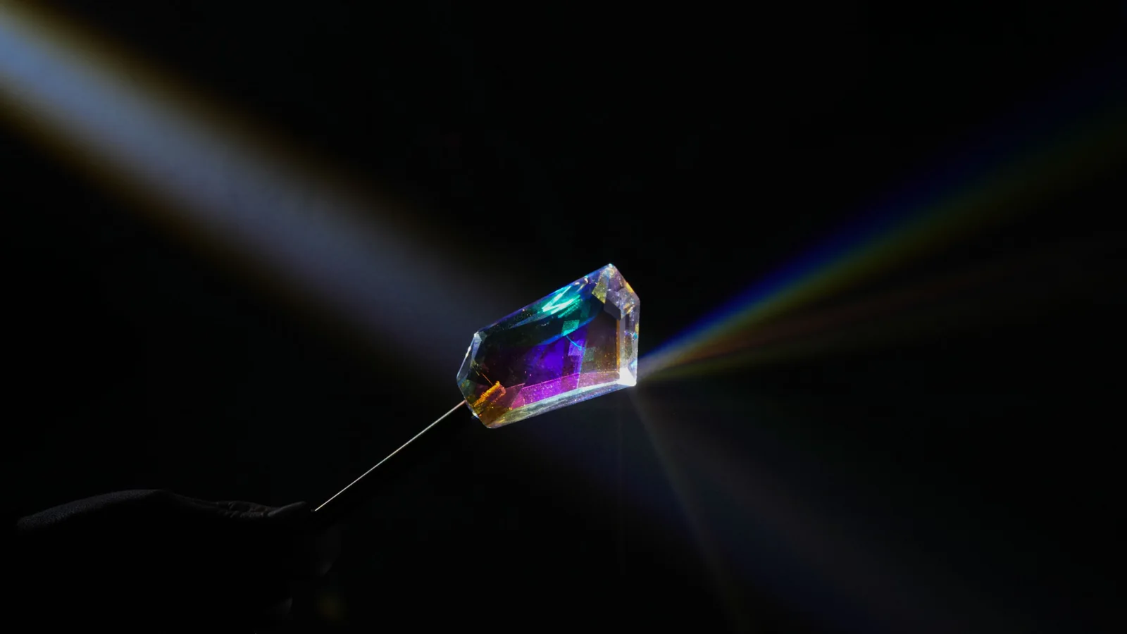 A hand holds a crystal prism in a white beam of light.
